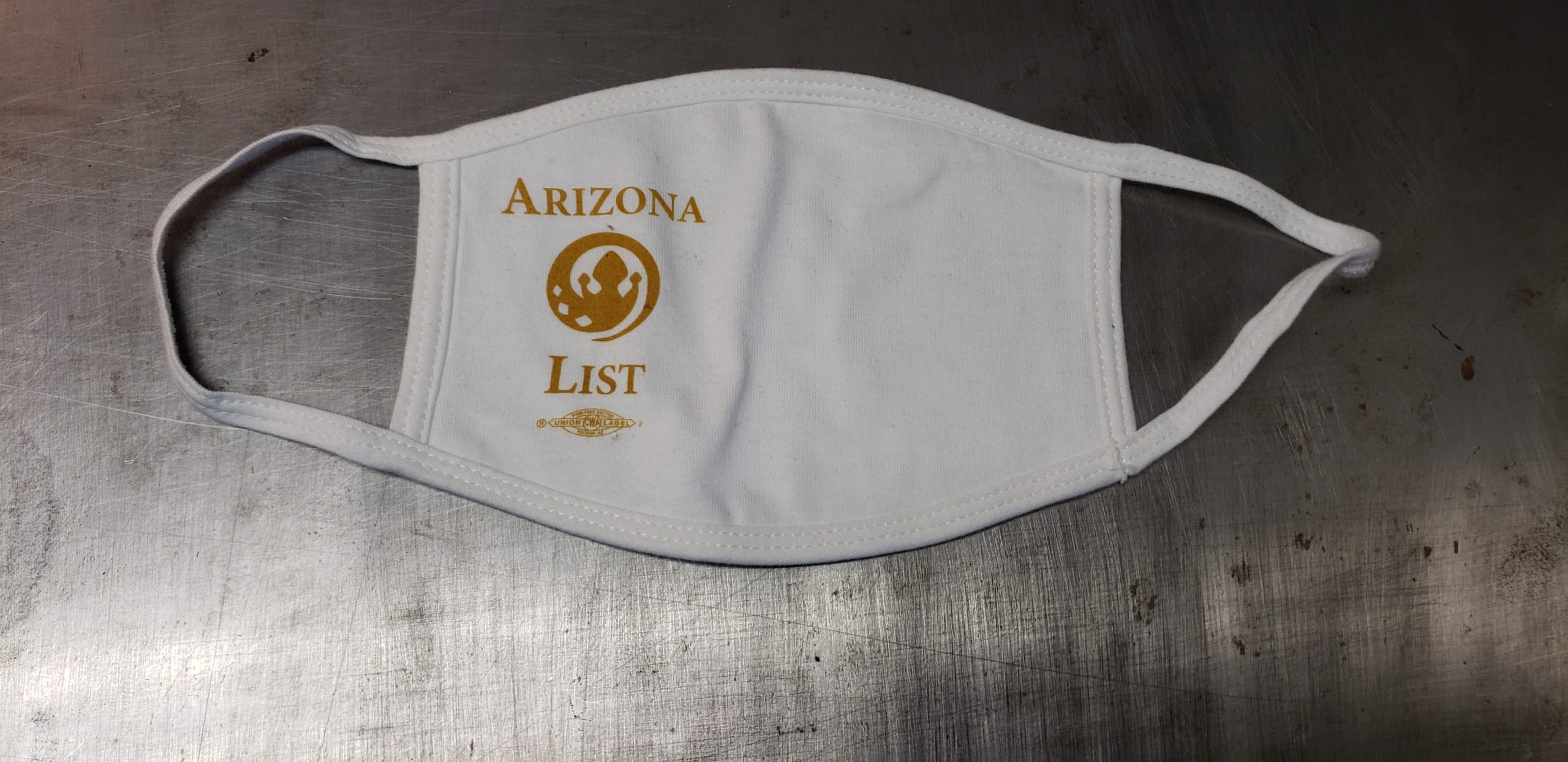 White cotton face mask with union screen printed one color design reading, "ARIZONA LIST" around a circular spiraling logo of a spade/crown design.